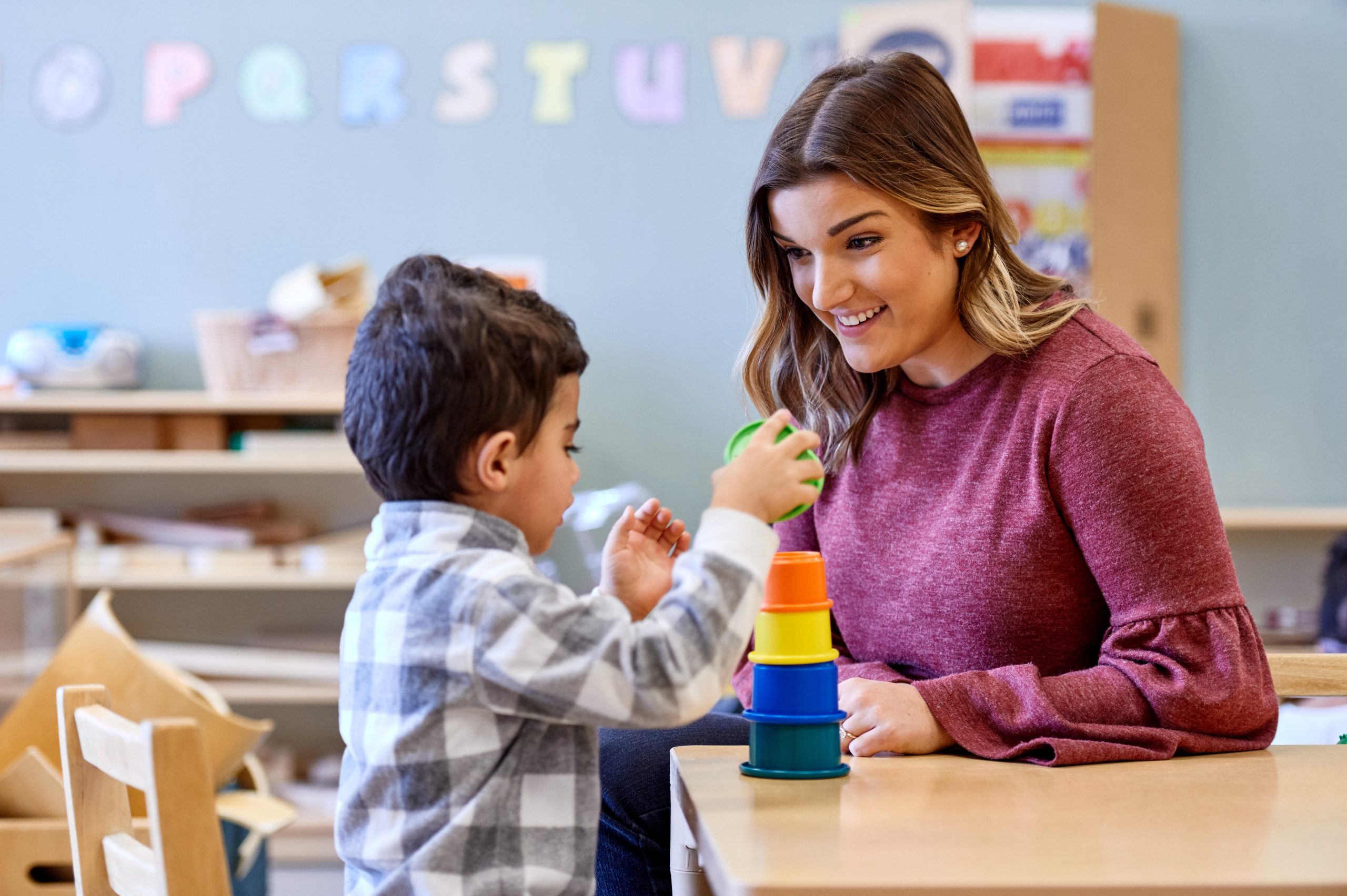 A teacher a child playing with stacking cups.